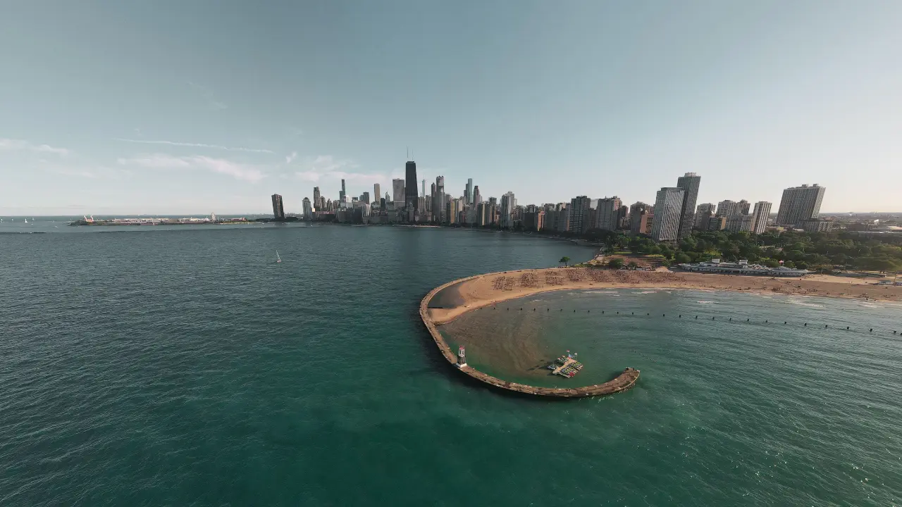 Aerial view of the Chicago skyline along Lake Michigan, with a curved breakwater and sandy beach in the foreground.