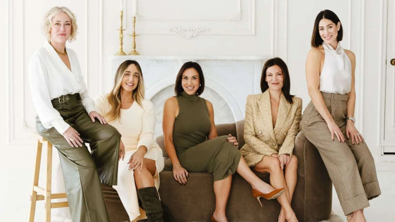 Group of five women from The Westhoff Group in Chicago in neutral-toned outfits posed together on and around a brown velvet sofa.