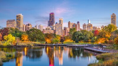 Lincoln Park with colorful fall trees and city skyline reflected in calm water.