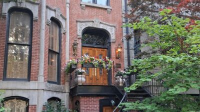 Brick brownstone entrance with a raised stoop and flower-lined railing.