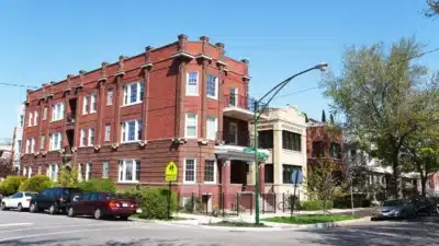 Three-story red brick corner apartment building with decorative columns and parked cars along the street in North Center, Chicago.