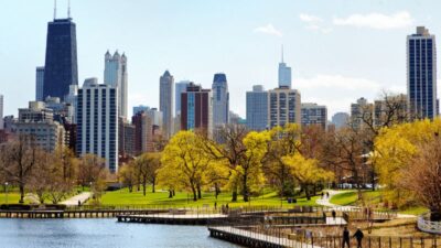 A lakeside path winds through a park with spring trees and a clear view of the Chicago skyline.