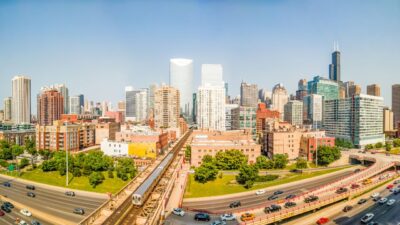 West Loop skyline with elevated train tracks and highway traffic on a sunny day.