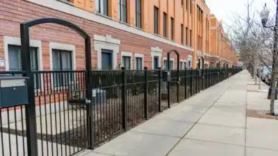 Row of red brick townhomes with black iron fencing along a tree-lined West Loop sidewalk.