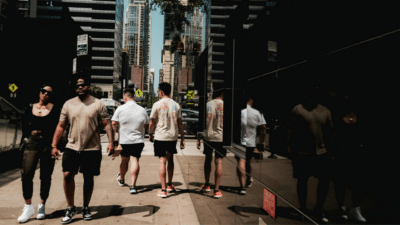 Pedestrians walking along a busy Chicago sidewalk with high-rise buildings and storefront reflections visible.