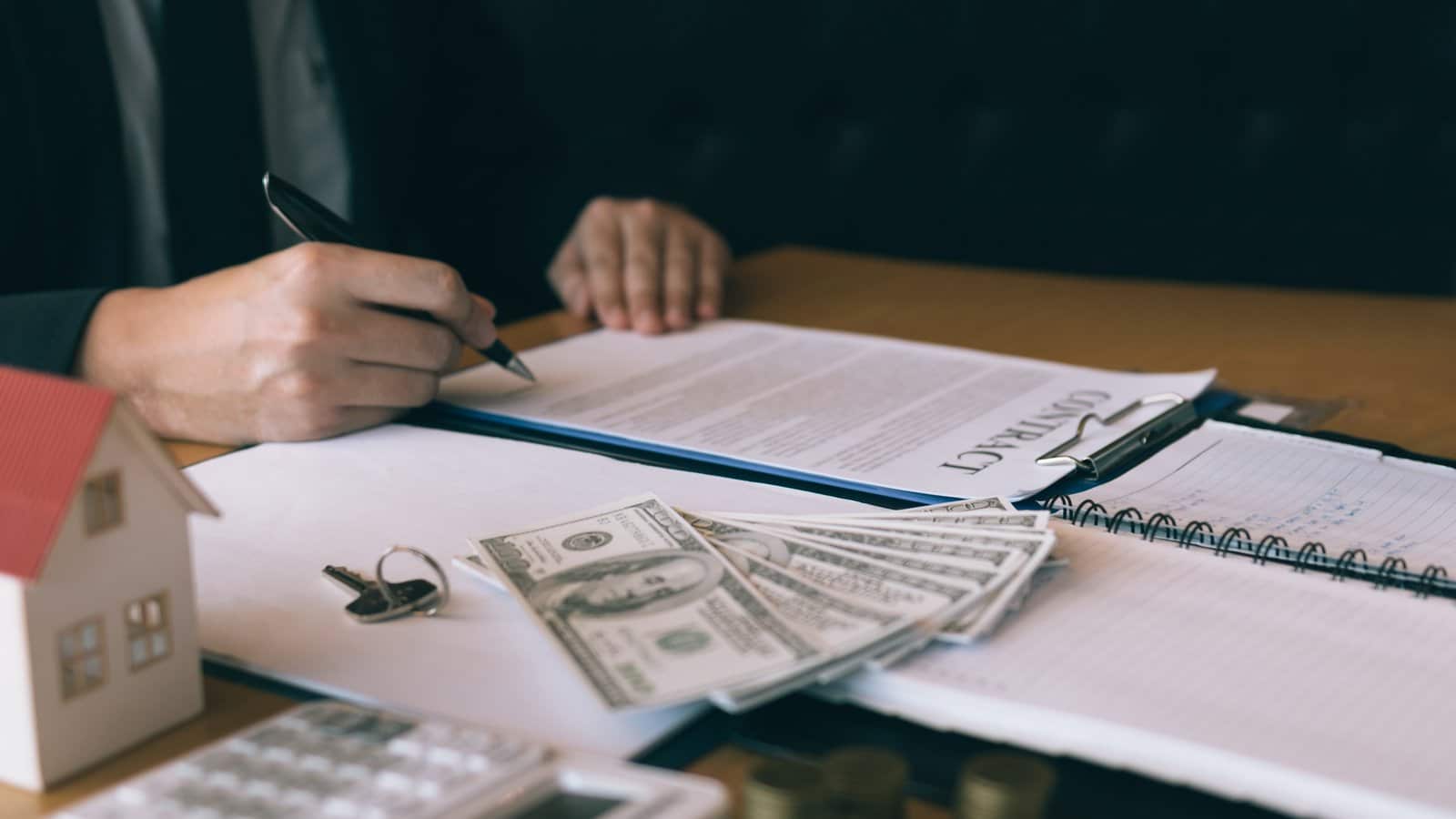 Buyer signing a home purchase contract next to cash and a calculator