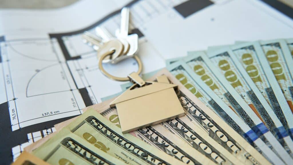 House keys with a house-shaped keychain resting on cash over a floor plan, representing Chicago closing costs
