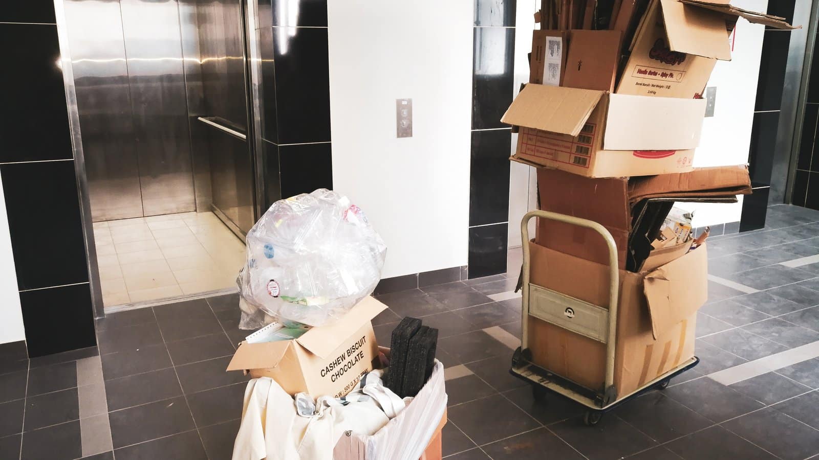 Moving boxes stacked on a cart beside a condo building elevator